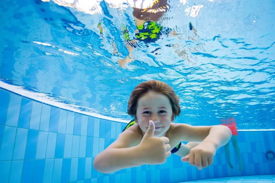 Ein Kind schwimmt unter Wasser und lächelt im Schwimmbad des Ostsee Resorts Damp.